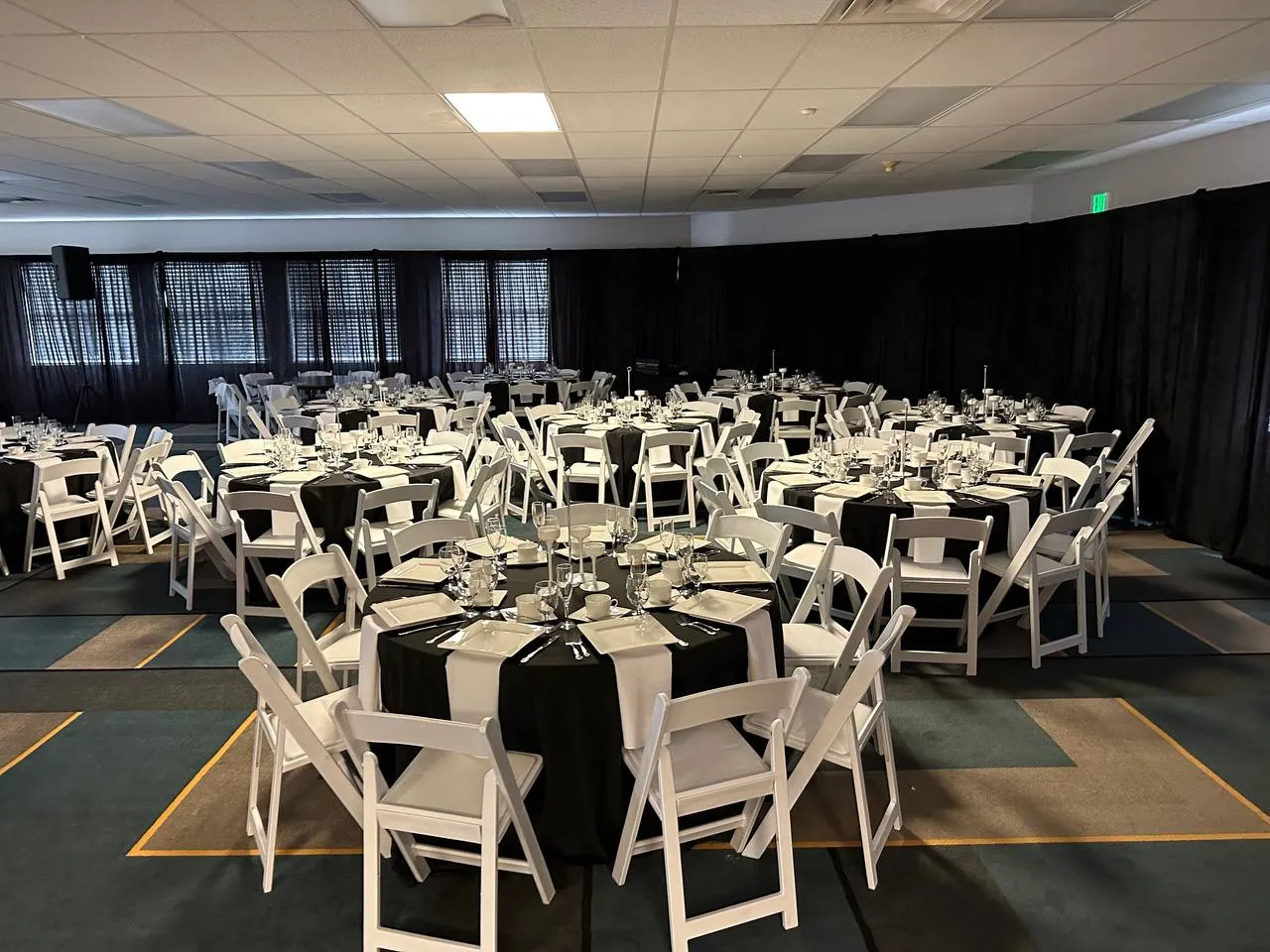 Banquet hall lined with black drapes and filled with round tables in black linens and white folding chairs