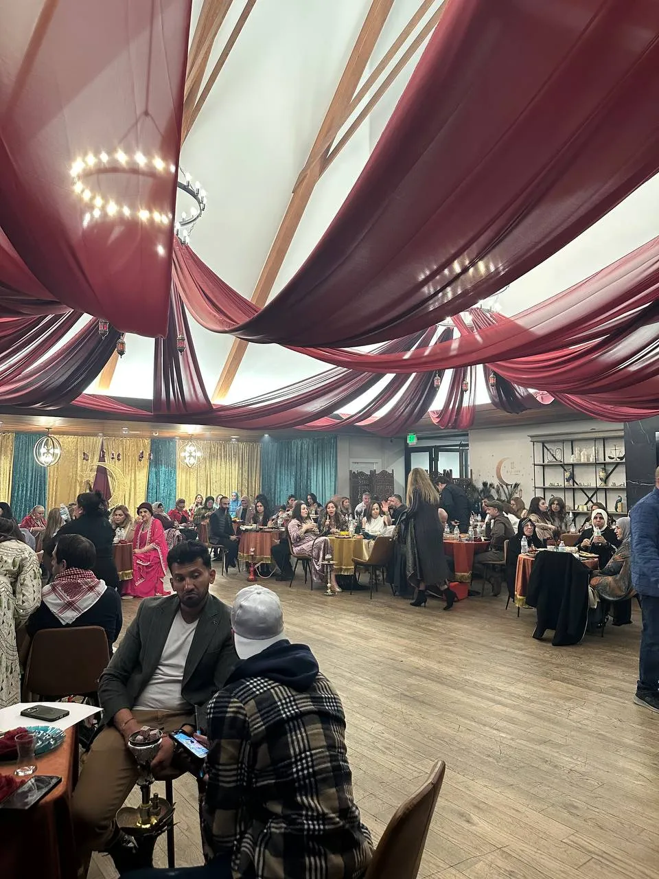 Guests at tables in a hall with burgundy fabric draped across the ceiling and ring chandeliers