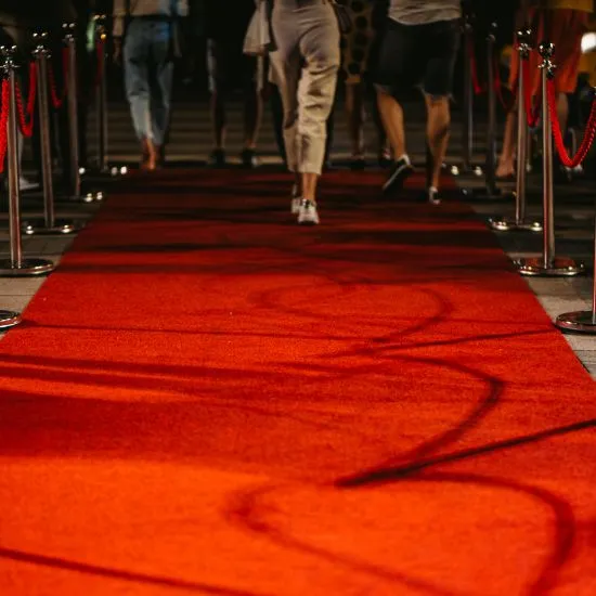 Red carpet lined with chrome stanchions and red velvet ropes as people walk along it