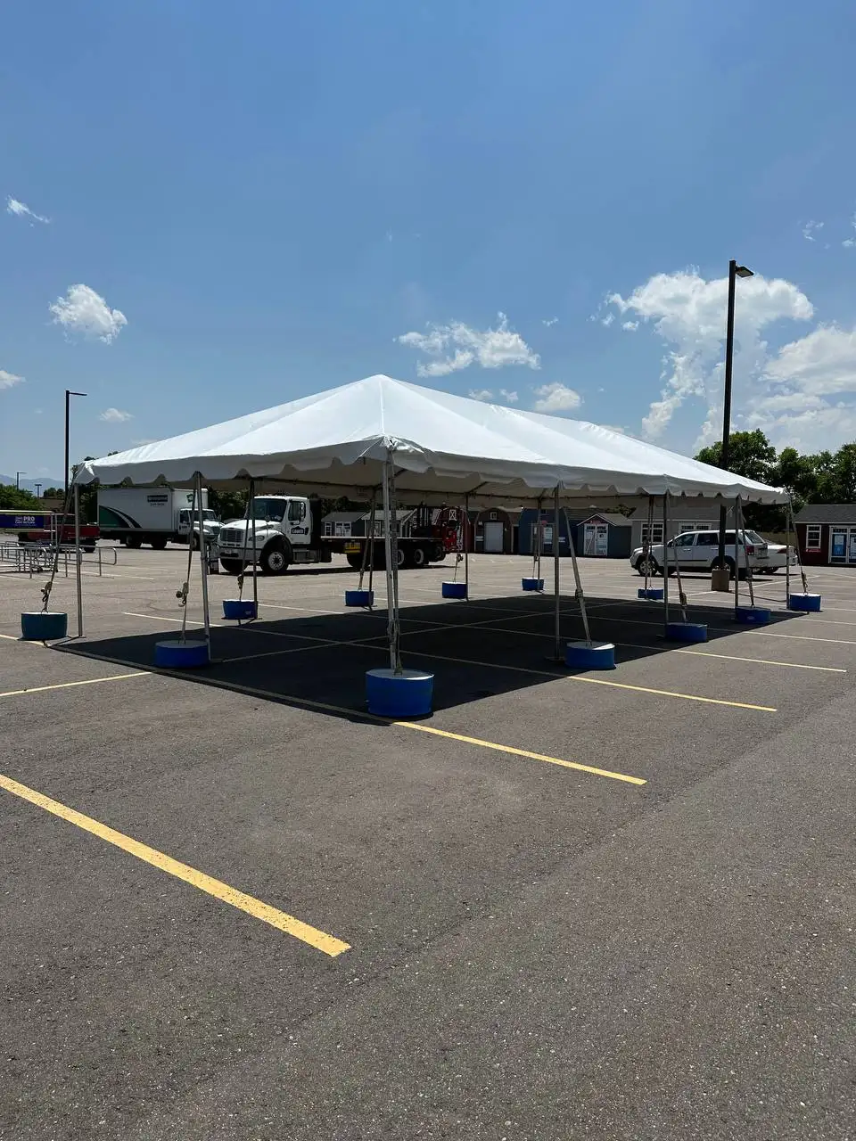 White frame tent on a parking lot, its legs set in blue water barrels, over black flooring