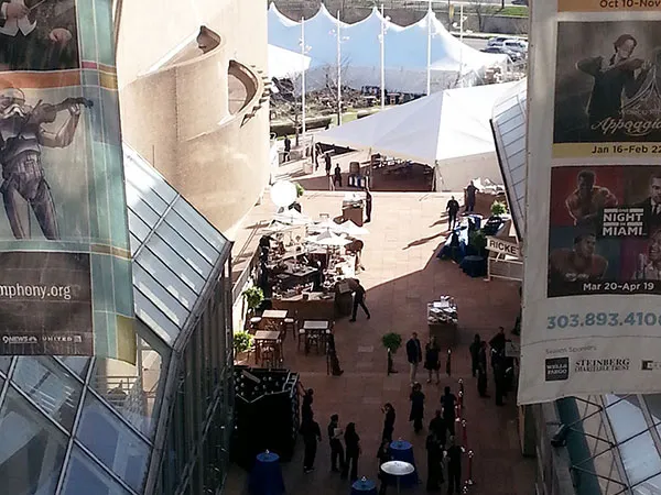 Elevated view of a plaza with white tents, tables with blue linens and people in dark clothing between glass office towers