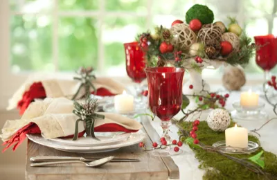 Table set with folded napkins on white plates, red glass goblets, candles on green moss and a red-berry centerpiece