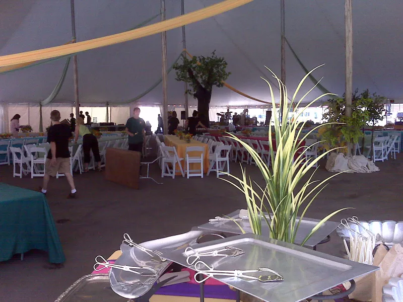 Large white tent interior with support poles, colorful linens, white folding chairs and draped fabric overhead, serving trays in front