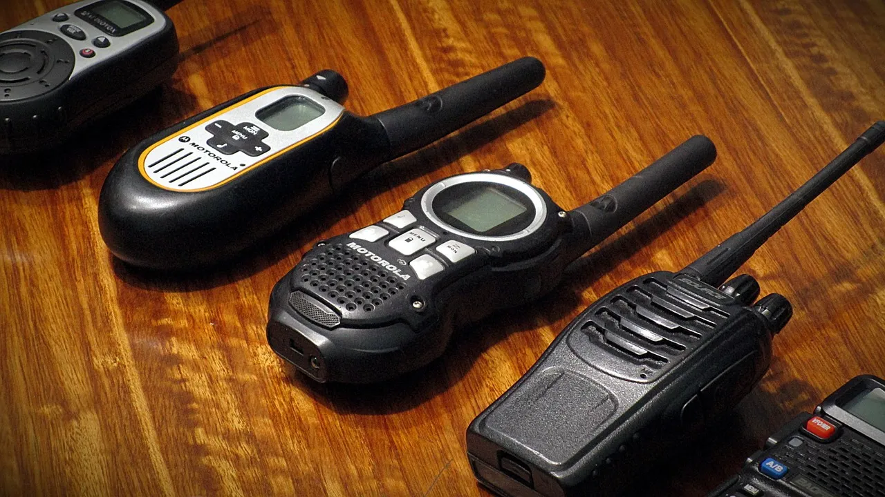 Handheld two-way radios with antennas, in different sizes, lying on a glossy wooden table