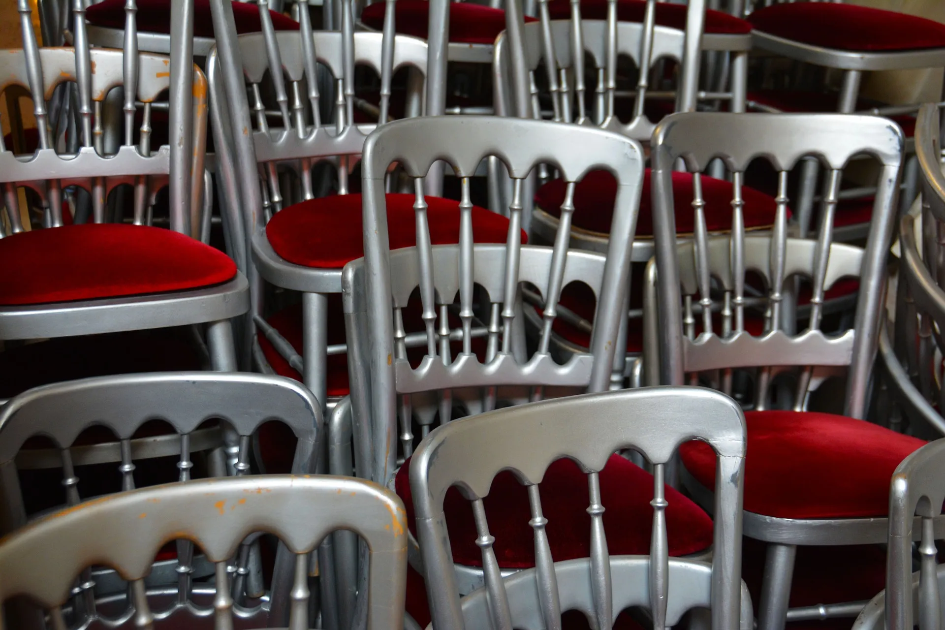 Close-up of silver chairs with red padded seats stacked and packed closely together