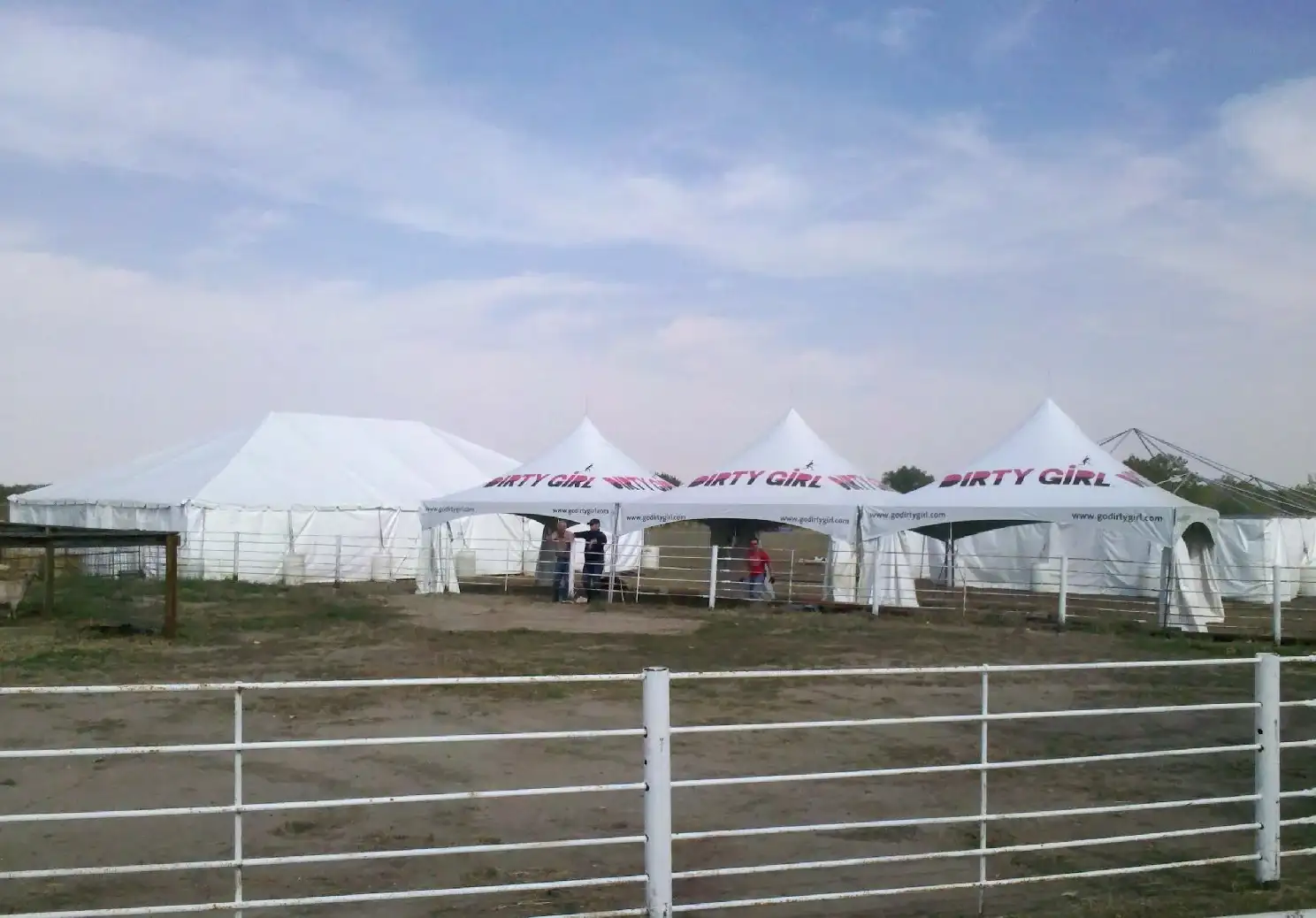 White tents with printed valances on a grass field behind a white rail fence