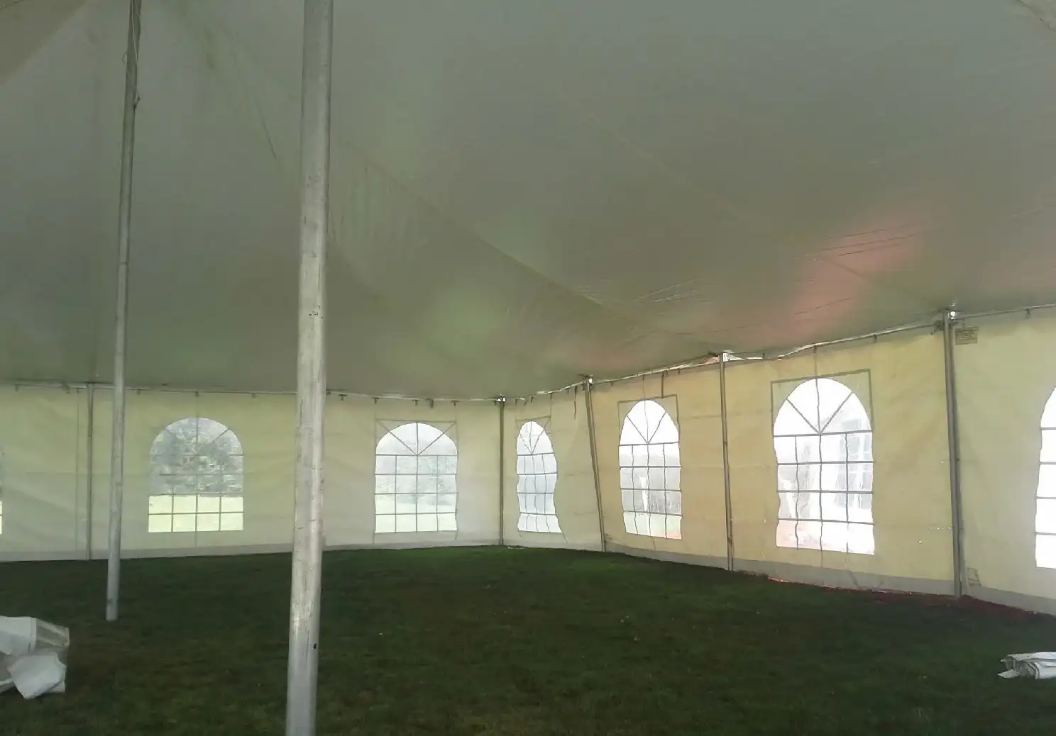 Pole tent interior with tall metal poles, cream sidewalls with arched windows and an empty grass floor