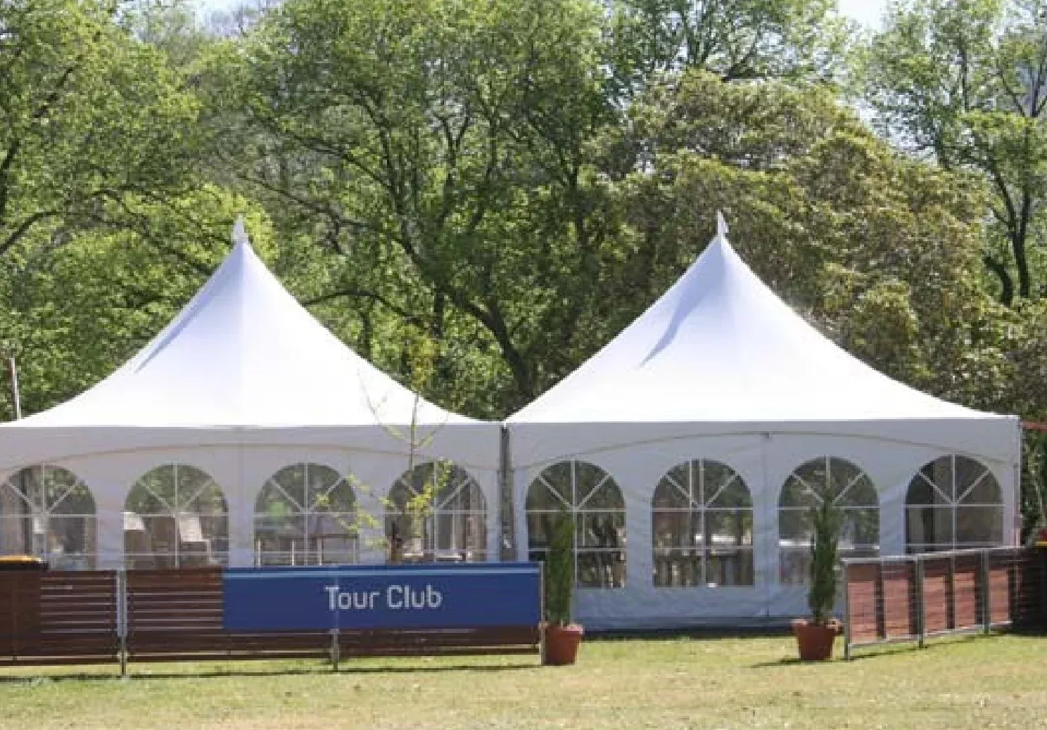 Two white high-peak tents joined side by side with arched window sidewalls, slatted wood fencing and potted evergreens