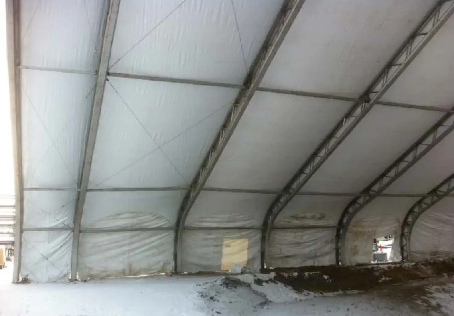 Inside a clearspan tent with arched aluminum truss ribs, white fabric walls and a snow-dusted dirt floor with a mound of soil
