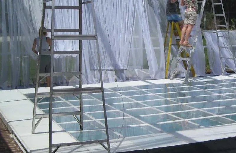 Workers on ladders hanging white drapes beside a clear-panel floor
