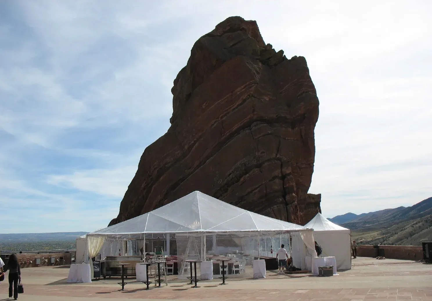 Clear-top frame tent with clear sidewalls and white-draped cocktail tables on a stone terrace below a huge red rock formation
